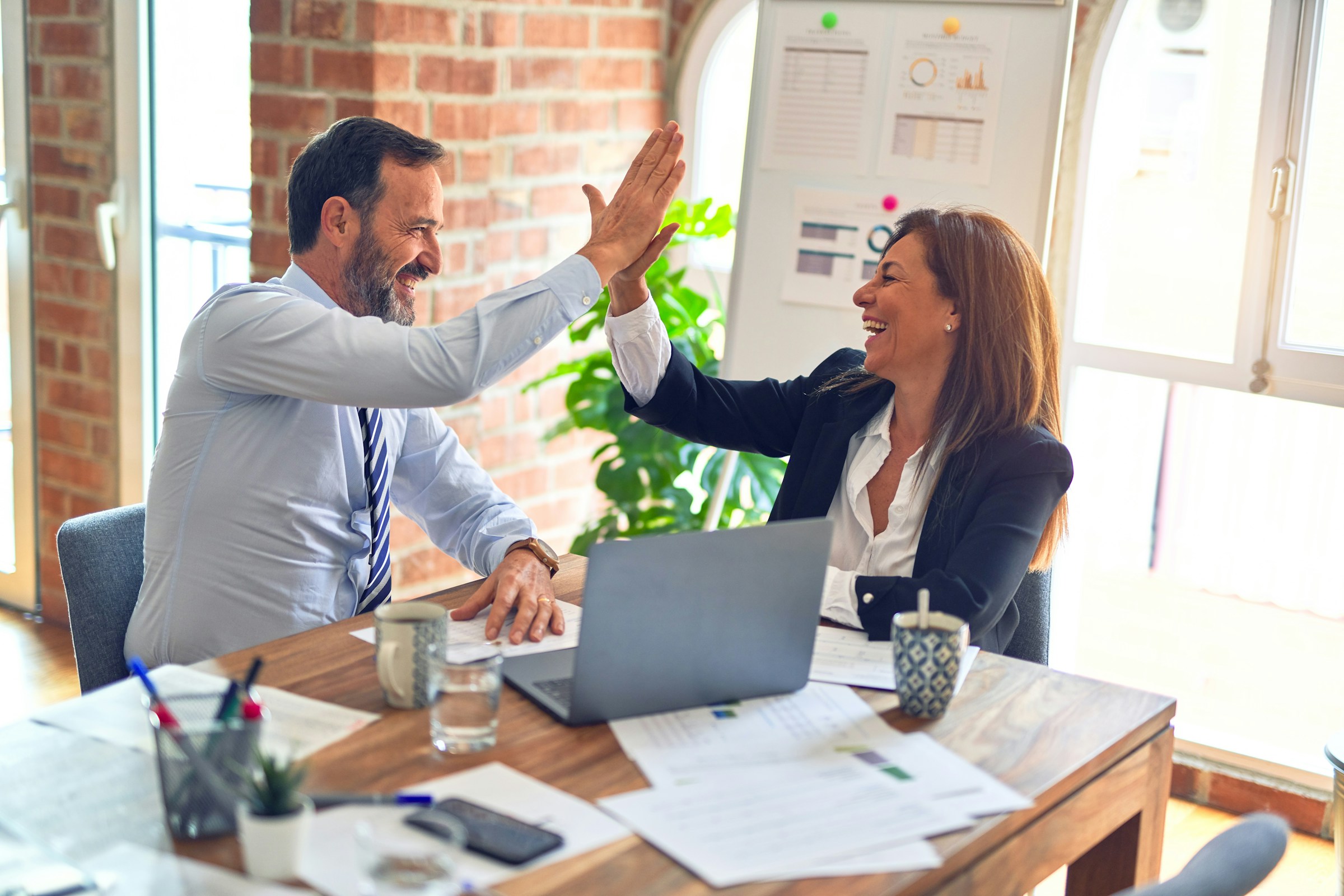 Two people give each other a high five while sitting down in a office setting.