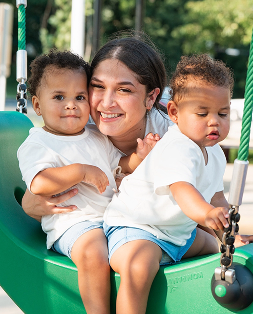 Woman with two children on a green swingset