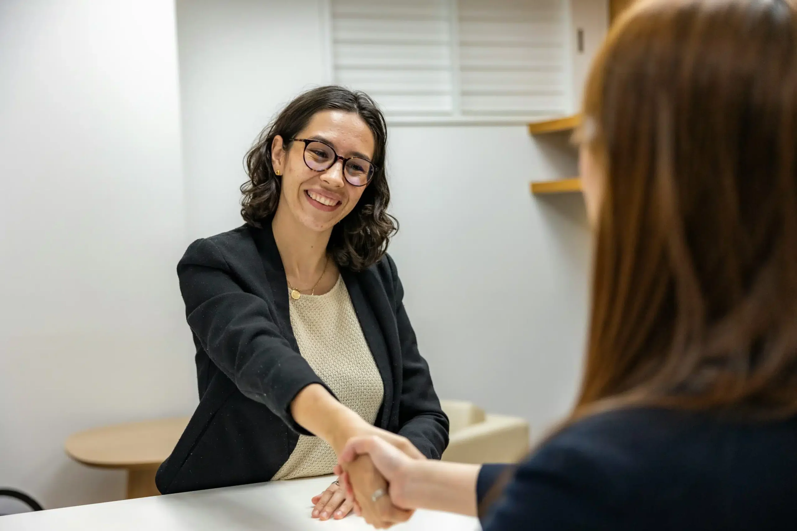 Over the shoulder shot of a young woman giving another a handshake.