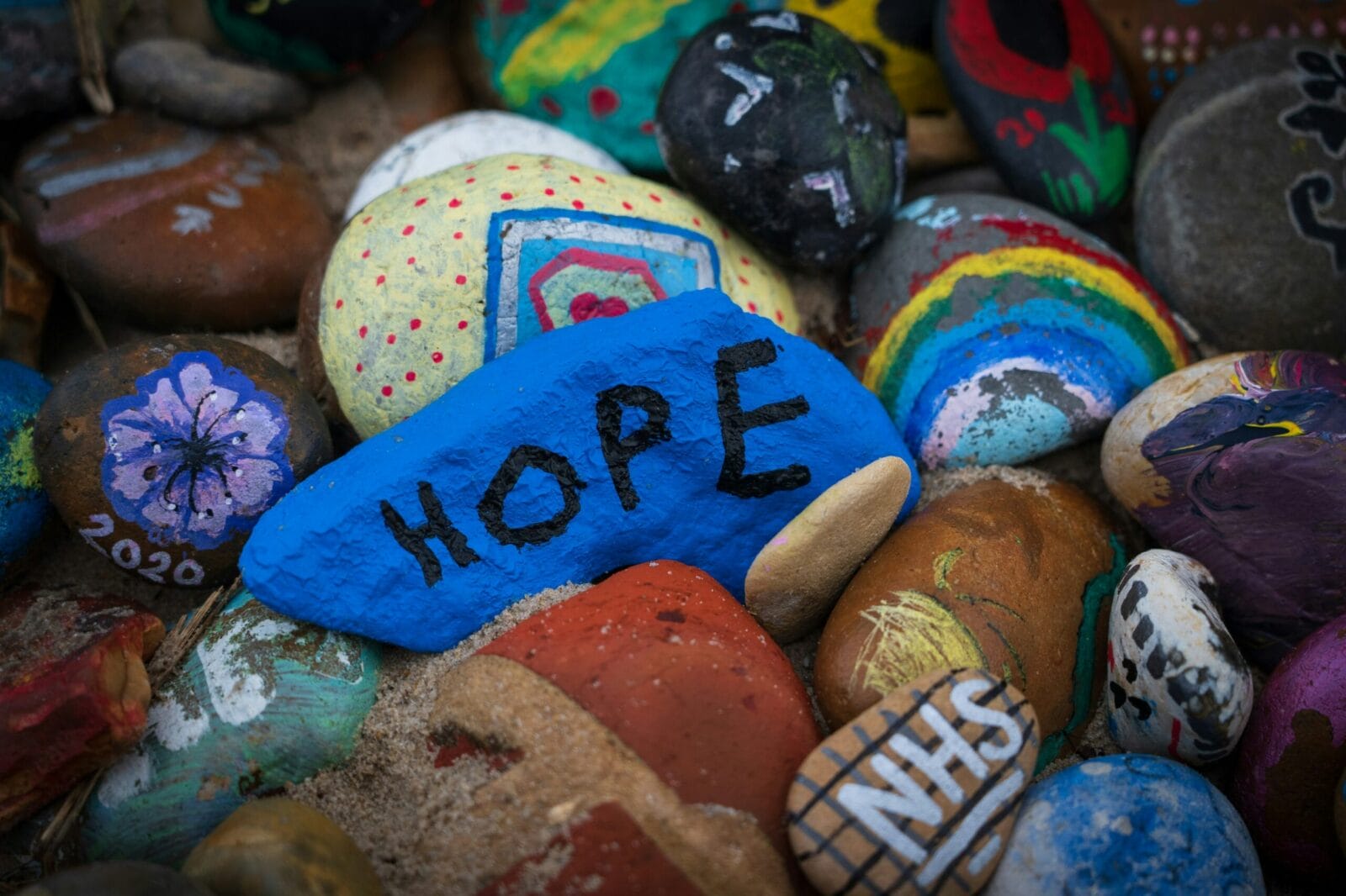Various colorful painted rocks with one blue one in the middle with "HOPE" in black paint